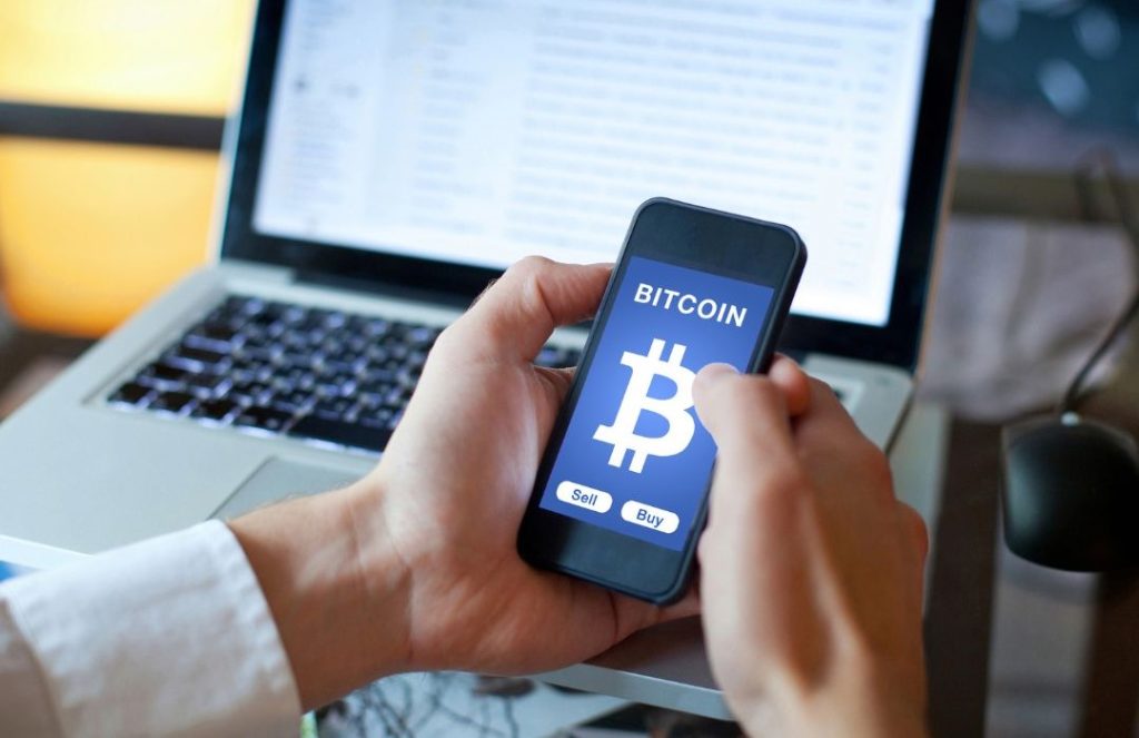 Osoba korzystająca z aplikacji mobilnej do kupna i sprzedaży Bitcoina, symbolizująca zarządzanie kryptowalutami w kontekście podatków. Przypomnienie o obowiązku rozliczenia kryptowalut w Niemczech oraz zapłacie podatku od kryptowalut w Niemczech.